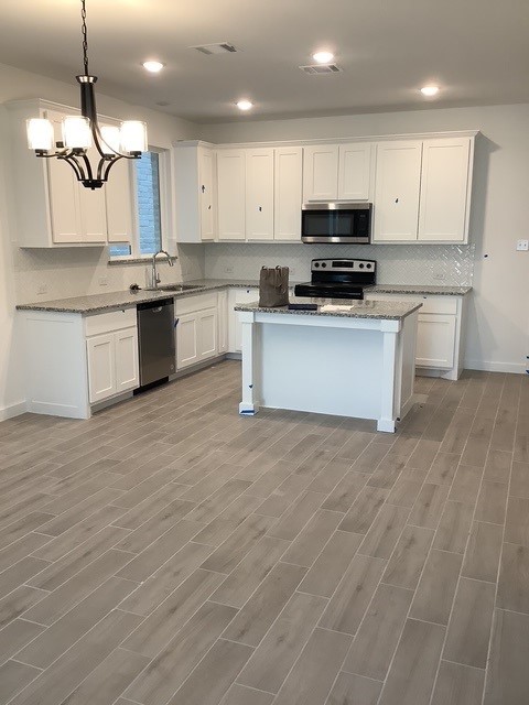 kitchen with white cabinetry, stainless steel appliances, light stone counters, pendant lighting, and a kitchen island