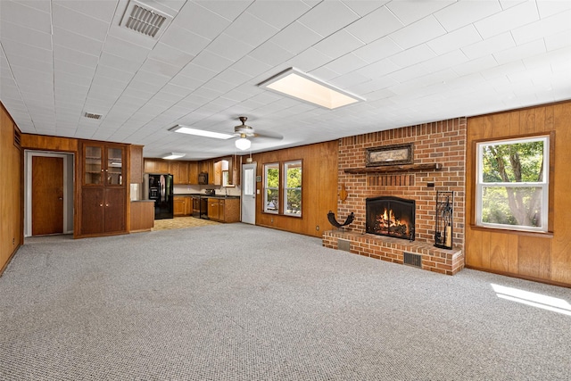 unfurnished living room with ceiling fan, a brick fireplace, light carpet, and wooden walls