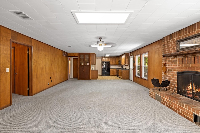 carpeted living room with ceiling fan, wooden walls, sink, and a fireplace