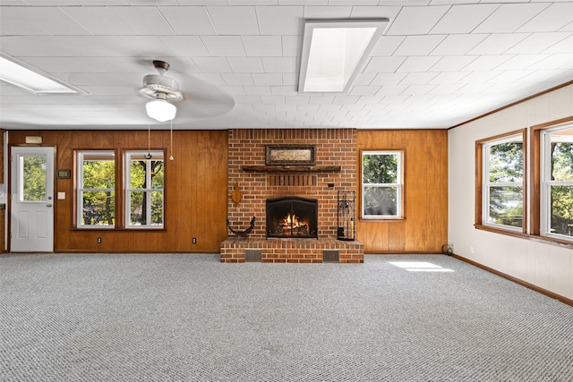 unfurnished living room with a brick fireplace, carpet floors, ceiling fan, and wood walls