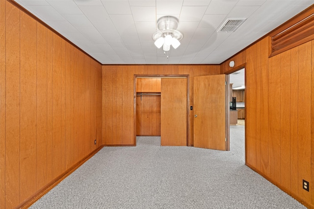 unfurnished bedroom with a closet, light colored carpet, and wood walls