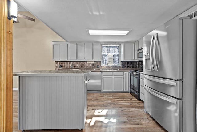 kitchen with kitchen peninsula, appliances with stainless steel finishes, light wood-type flooring, backsplash, and sink