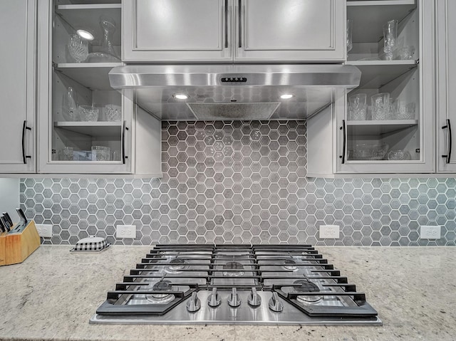 kitchen featuring stainless steel gas stovetop, light stone countertops, wall chimney range hood, and tasteful backsplash