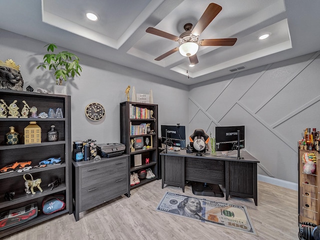 office space featuring a tray ceiling, ceiling fan, and light hardwood / wood-style flooring