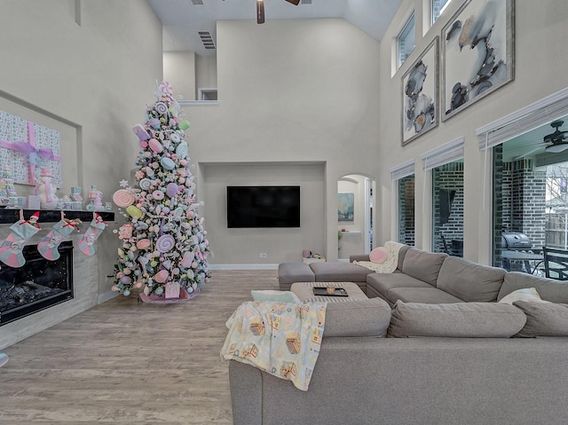 living room with ceiling fan, plenty of natural light, wood-type flooring, and a high ceiling