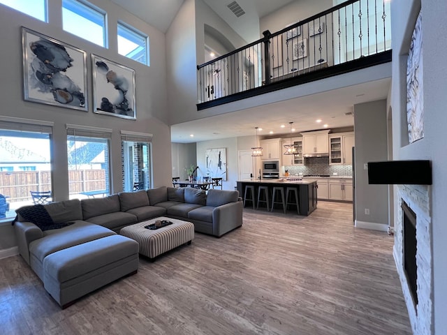 living room featuring a stone fireplace, a towering ceiling, and hardwood / wood-style floors