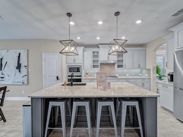 kitchen featuring a kitchen breakfast bar, stainless steel appliances, a spacious island, pendant lighting, and white cabinetry