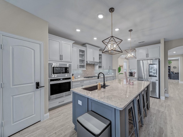 kitchen featuring light stone counters, stainless steel appliances, pendant lighting, a center island with sink, and white cabinetry