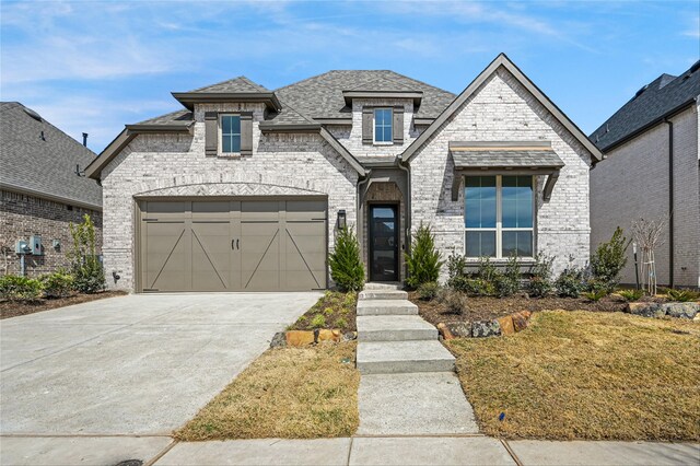 french country home with brick siding, roof with shingles, a garage, stone siding, and driveway