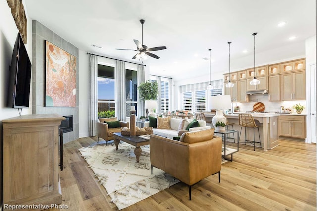 living room featuring ceiling fan, a tiled fireplace, and light hardwood / wood-style flooring