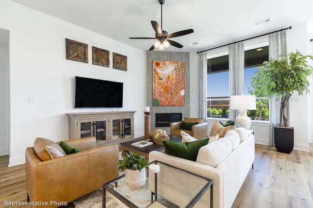 living room with ceiling fan, a tile fireplace, and light wood-type flooring