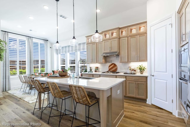 kitchen featuring a center island with sink, appliances with stainless steel finishes, sink, and hanging light fixtures