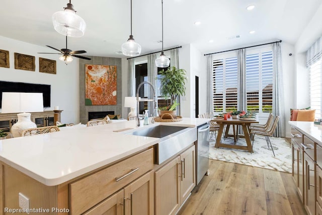 kitchen with sink, decorative light fixtures, a tiled fireplace, and an island with sink