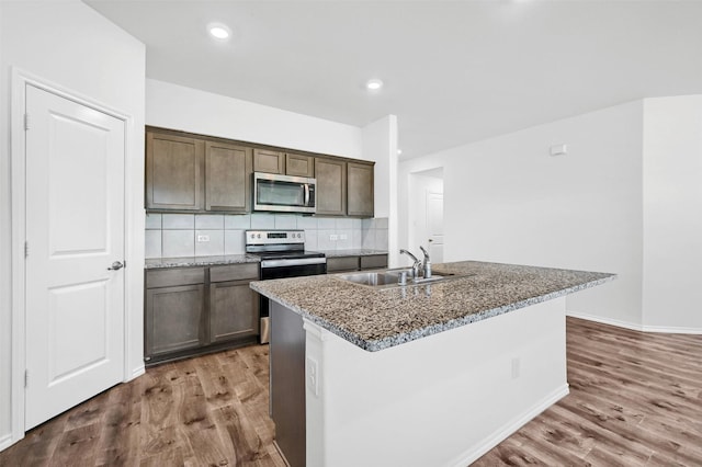 kitchen featuring sink, tasteful backsplash, dark stone countertops, a center island with sink, and appliances with stainless steel finishes