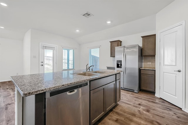 kitchen featuring light stone countertops, appliances with stainless steel finishes, a kitchen island with sink, sink, and wood-type flooring