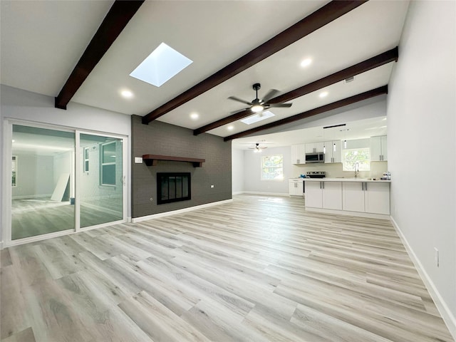 unfurnished living room with lofted ceiling with skylight, a fireplace, sink, ceiling fan, and light hardwood / wood-style flooring