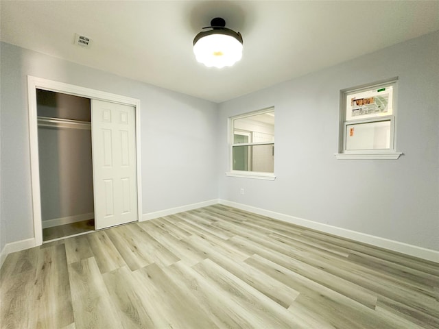 unfurnished bedroom featuring multiple windows, light hardwood / wood-style floors, and a closet