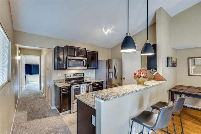 kitchen featuring kitchen peninsula, hanging light fixtures, appliances with stainless steel finishes, light stone counters, and a kitchen bar