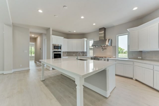 kitchen with white cabinetry, stainless steel appliances, sink, and wall chimney range hood