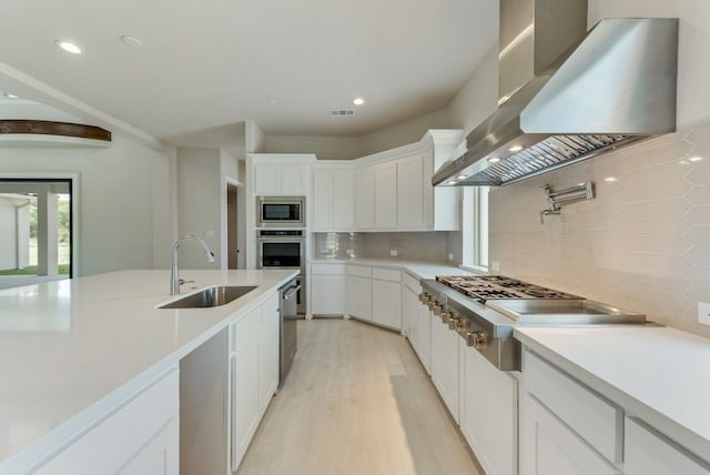 kitchen featuring white cabinetry, sink, stainless steel appliances, and wall chimney exhaust hood