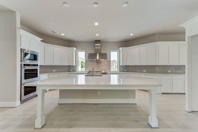 kitchen with white cabinetry, appliances with stainless steel finishes, wall chimney exhaust hood, and a large island