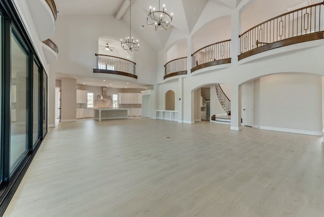 unfurnished living room featuring an inviting chandelier, a towering ceiling, and light wood-type flooring