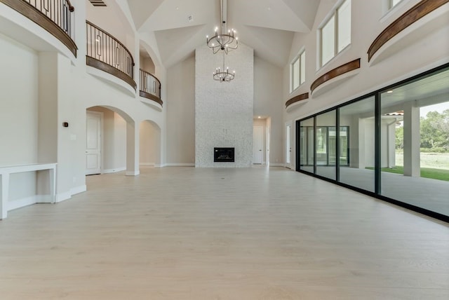 unfurnished living room featuring a high ceiling, a large fireplace, an inviting chandelier, and light hardwood / wood-style flooring