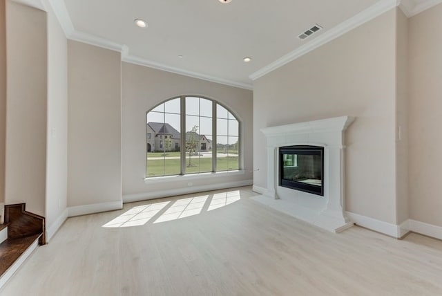 unfurnished living room featuring a tiled fireplace, crown molding, and light hardwood / wood-style floors