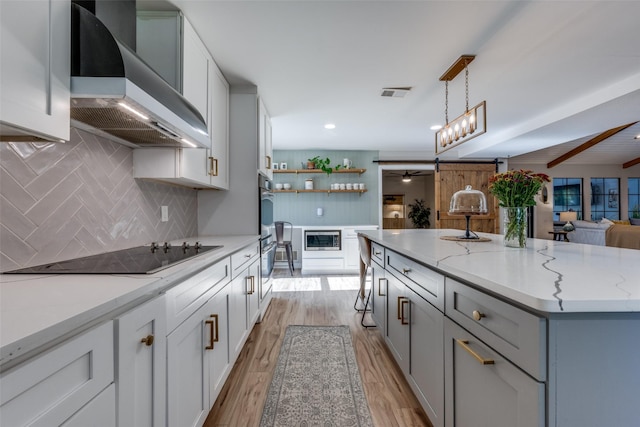 kitchen featuring decorative light fixtures, light stone counters, stainless steel appliances, wall chimney range hood, and light hardwood / wood-style flooring