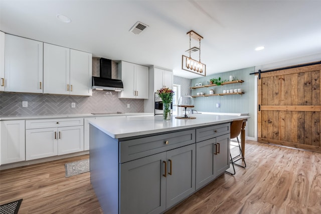 kitchen featuring white cabinetry, wall chimney range hood, an island with sink, and a barn door