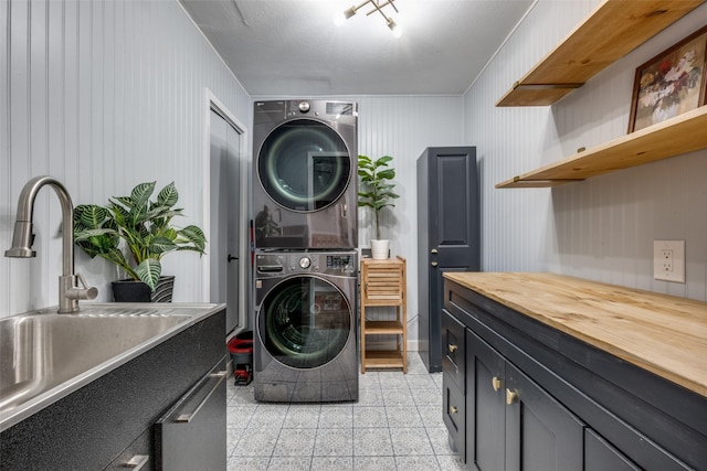 clothes washing area with cabinets, stacked washer and clothes dryer, and sink