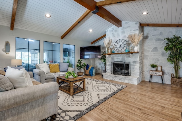 living room with lofted ceiling with beams, a stone fireplace, and light wood-type flooring