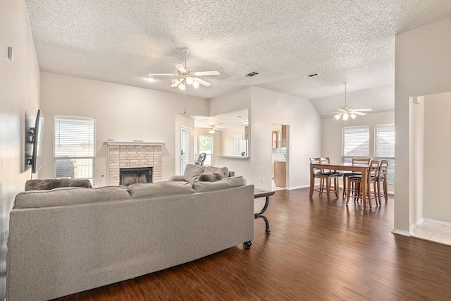 living room with lofted ceiling, a brick fireplace, dark hardwood / wood-style floors, ceiling fan, and a textured ceiling