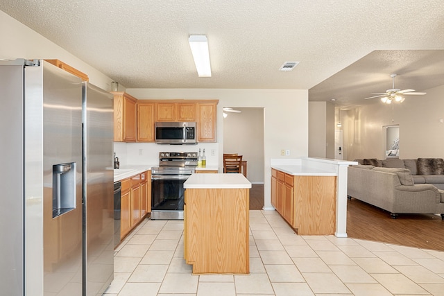 kitchen with a center island, ceiling fan, a textured ceiling, light tile patterned flooring, and stainless steel appliances