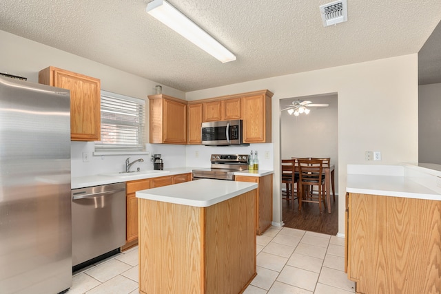 kitchen with a textured ceiling, a center island, light tile patterned floors, and stainless steel appliances