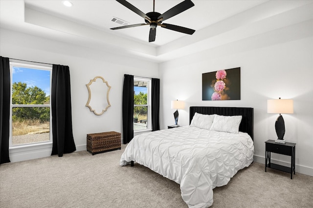 carpeted bedroom with ceiling fan and a raised ceiling