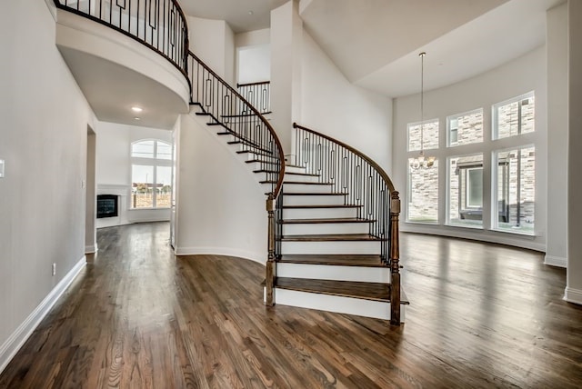 stairs with a towering ceiling, wood-type flooring, and a notable chandelier