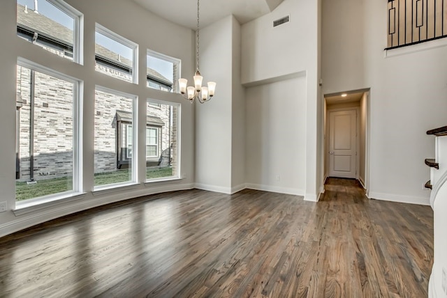 unfurnished dining area with dark wood-type flooring, a towering ceiling, and a notable chandelier