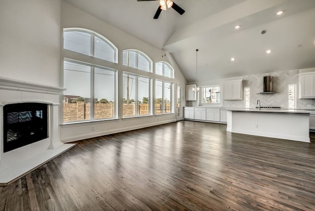 unfurnished living room with dark wood-type flooring, ceiling fan, sink, and vaulted ceiling