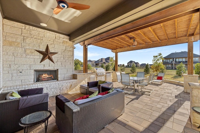 view of patio with an outdoor living space with a fireplace, ceiling fan, area for grilling, and an outdoor kitchen