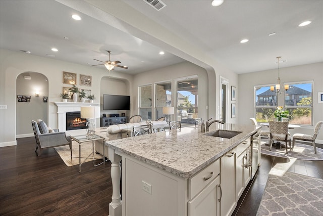 kitchen with sink, white cabinets, hanging light fixtures, light stone countertops, and a center island with sink