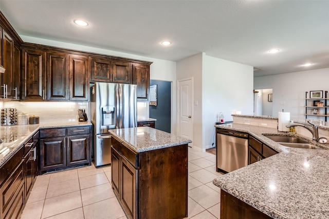 kitchen with light stone countertops, appliances with stainless steel finishes, dark brown cabinets, sink, and a center island