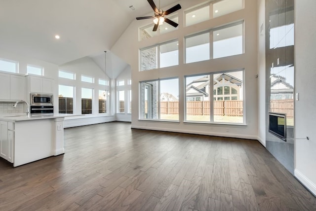 unfurnished living room featuring ceiling fan, sink, dark hardwood / wood-style flooring, and high vaulted ceiling