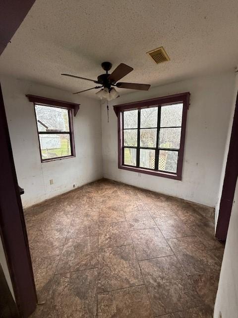 empty room featuring ceiling fan, plenty of natural light, and a textured ceiling