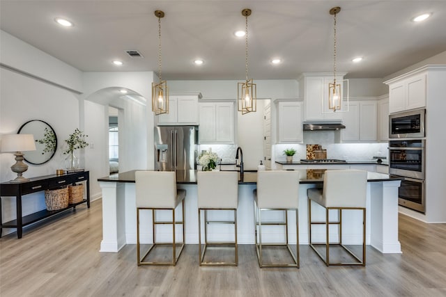 kitchen with decorative light fixtures, white cabinetry, stainless steel appliances, and an island with sink