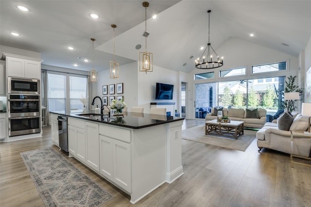 kitchen with built in microwave, sink, decorative light fixtures, a center island with sink, and white cabinets