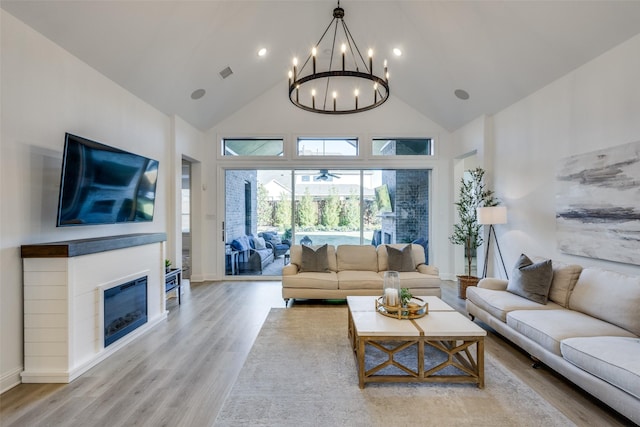 living room with a notable chandelier, light wood-type flooring, and high vaulted ceiling