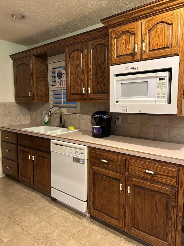 kitchen featuring backsplash, white appliances, sink, and a textured ceiling