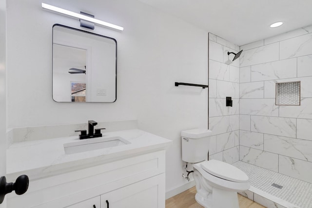 bathroom with a tile shower, hardwood / wood-style floors, vanity, and toilet