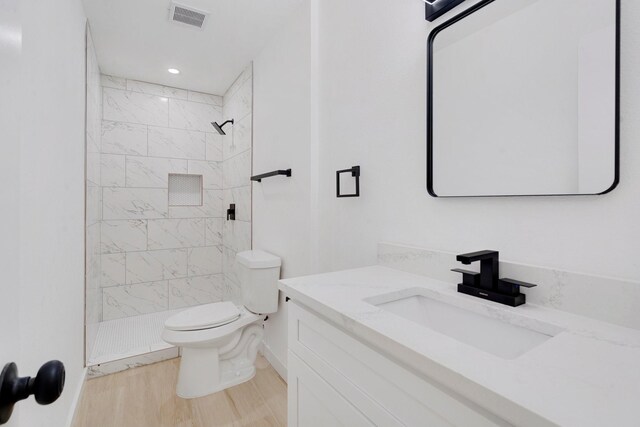 bathroom featuring tiled shower, hardwood / wood-style floors, vanity, and toilet